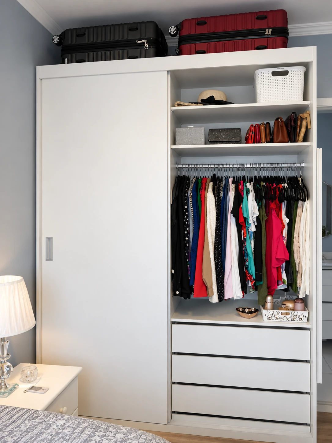 Guarda-roupa com roupas penduradas por cor, bolsas na prateleira e malas em cima
